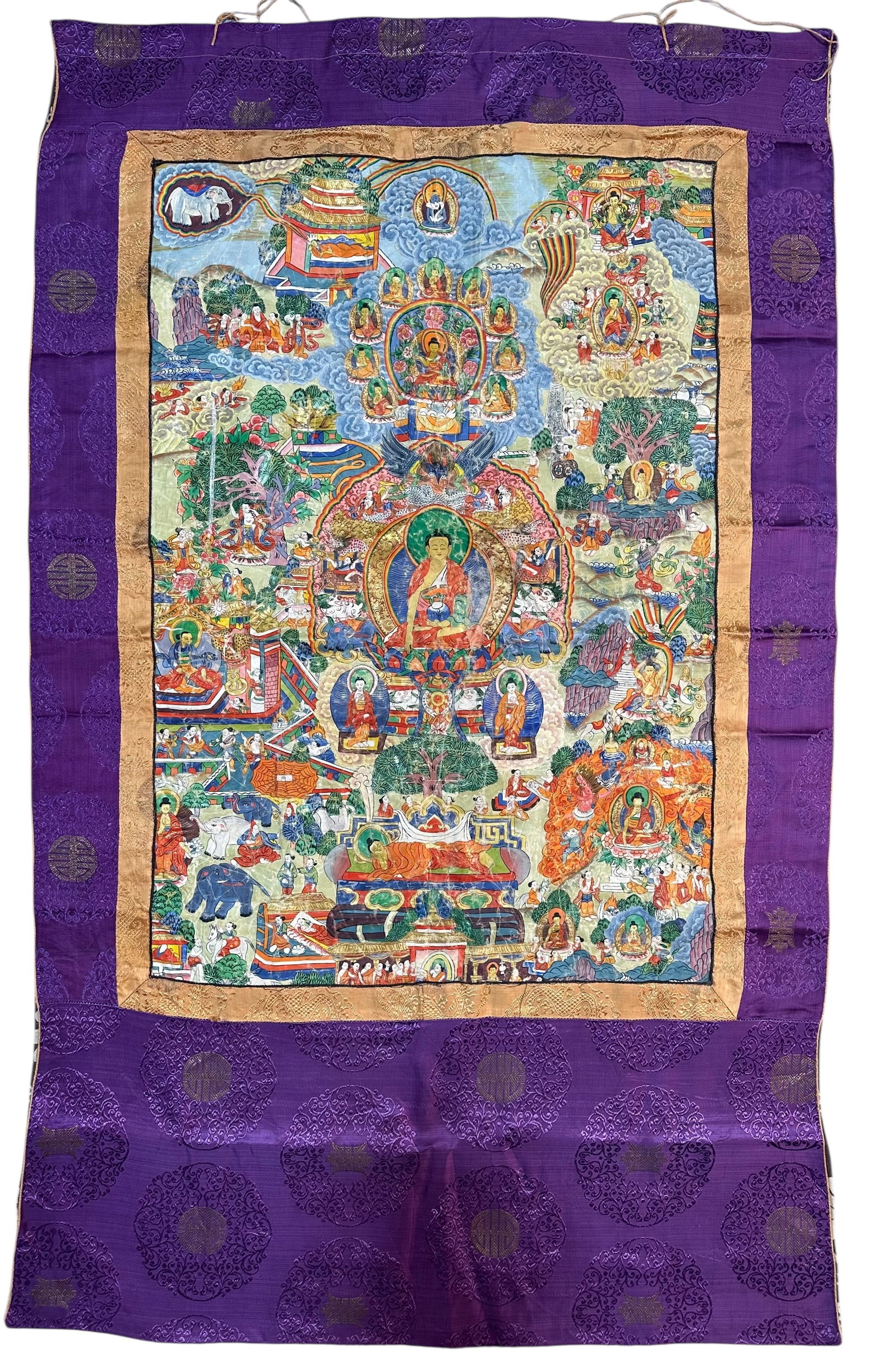 Antique Antique Traditional Tibetan Thangka Painting Of The Buddhas Life Story Circa 1900: Antique Traditional Tibetan Thangka Painting Of The Buddhas Life Story, featuring detailed hand-painted iconography mounted within a purple silk brocade border circa 1900. size: 116 cm x 69 cm (46ins 