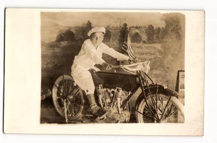 Sepia Real Photo Postcard: Young Boy in Cap and Knickers on Motorcycle with US Flag Backdrop