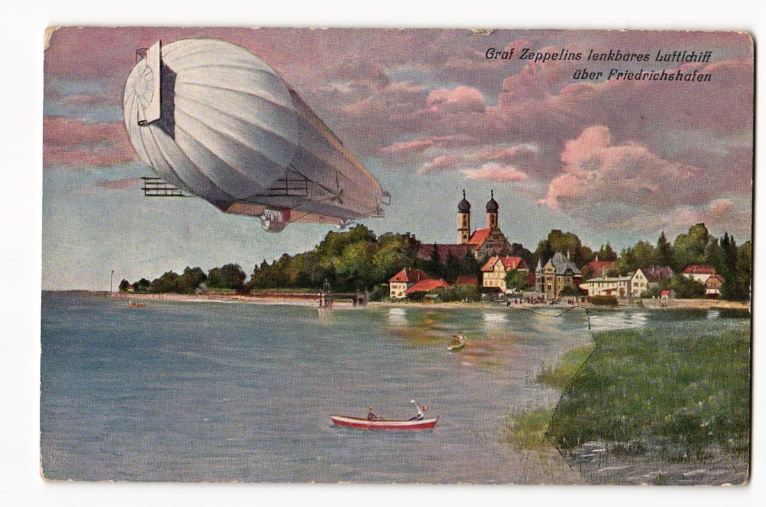 Graf Zeppelin airship flying over Friedrichshafen, lakeside town view, early 20th century.: The front of the postcard features a color illustration depicting the Graf Zeppelin airship in flight, angled from left to right, over a body of water. Below the airship, on the shore, is a town ident