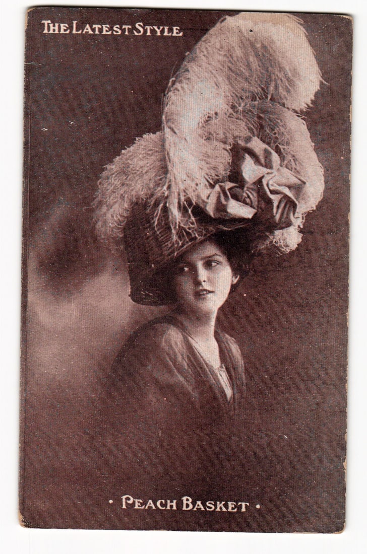 Woman in "Peach Basket" Hat, "The Latest Style" Series, Early 20th Century Portraiture: The front of the postcard features a tinted photographic portrait of a woman. She is depicted from the bust up, facing slightly to her right, with her gaze directed towards the viewer. Her dark hair i