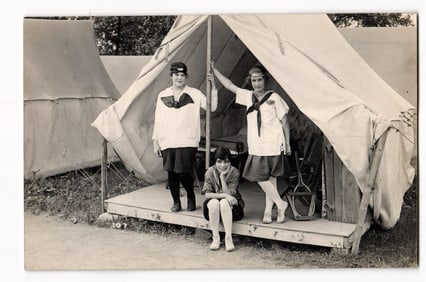 Real Photo Postcard: Three Young Women in Uniforms Posing at Tent Entrance, Camp Setting.