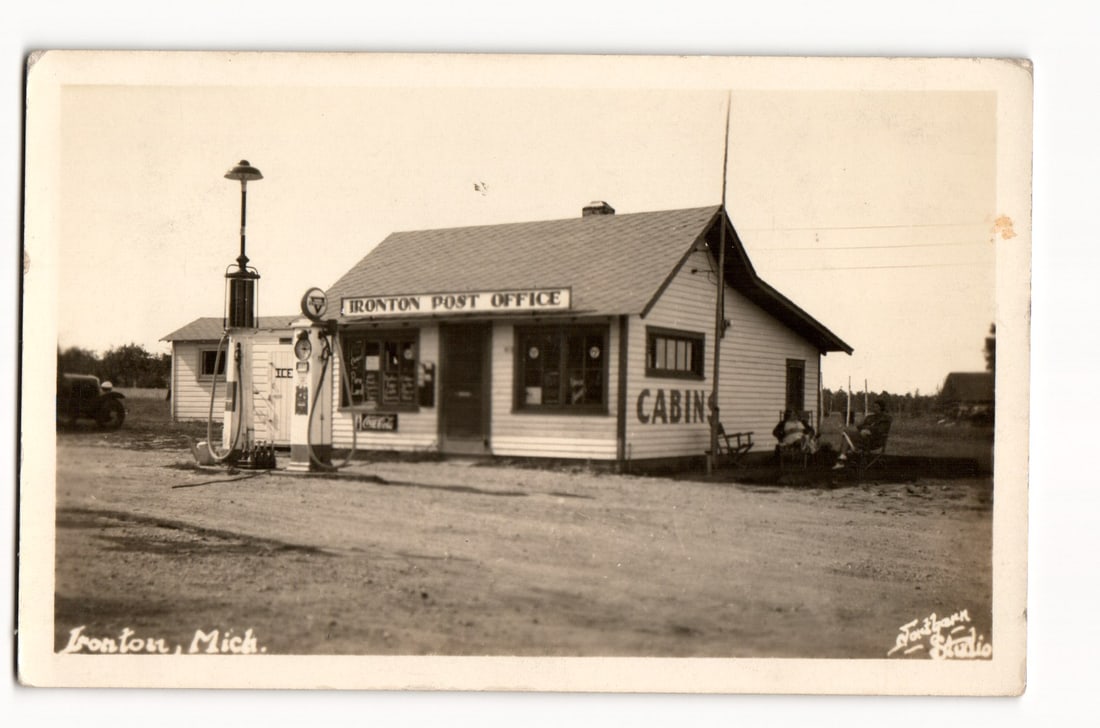 Ironton Post Office and Cabins with Gas Pump, Automobile, Ironton, Michigan, circa 1937 RPPC: Description:The front of this Real Photo Postcard (RPPC) presents a sepia-toned, eye-level photographic image. The central subject is a single-story wooden building, distinguished by a sign above the