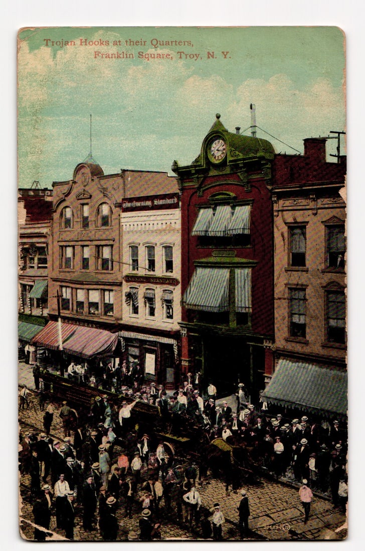 Trojan Hooks at their Quarters, Franklin Square, Troy, N.Y.; Busy Street Scene, ca. 1912: The front of this color postcard depicts a bustling street scene at Franklin Square, Troy, N.Y. The image shows a crowd of people, predominantly men in period attire including hats, gathered on a cobb