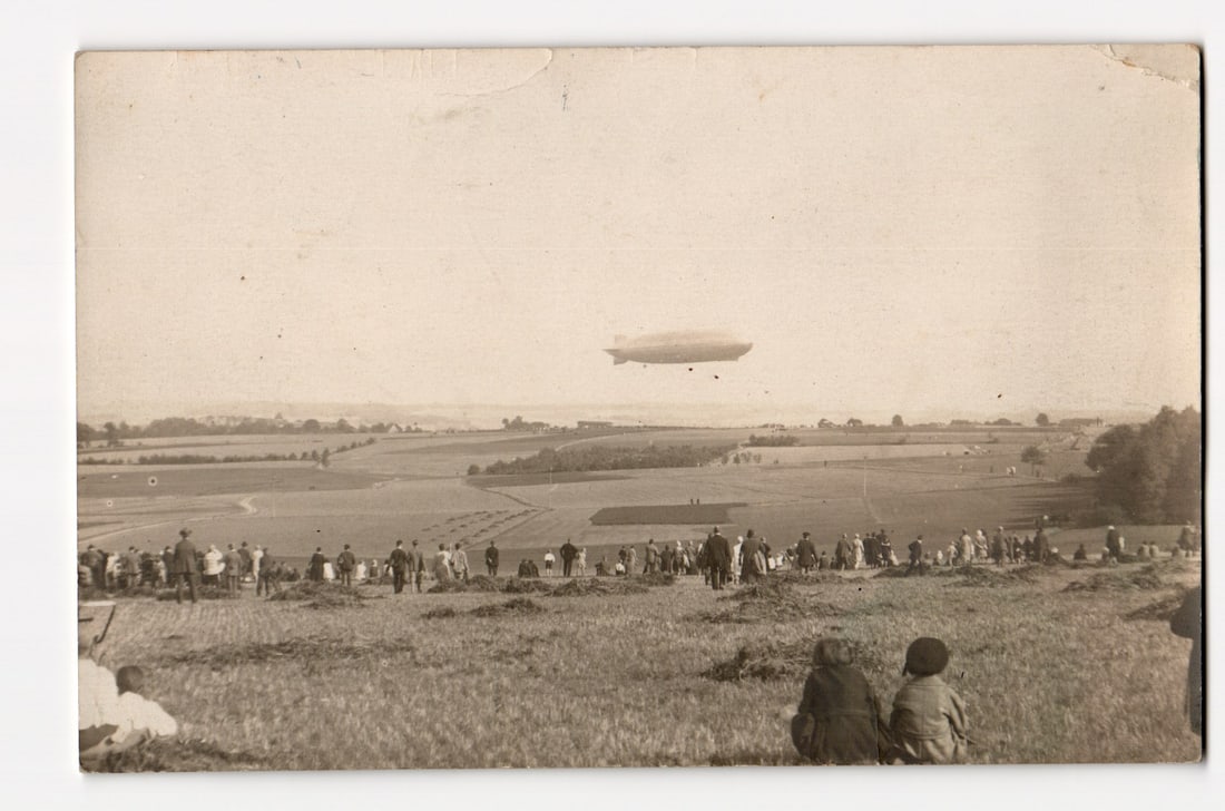 Real Photo Postcard: Airship (Dirigible) Flying Over Field, Spectators Gathered Below, c. 1910s. (1 of 2)