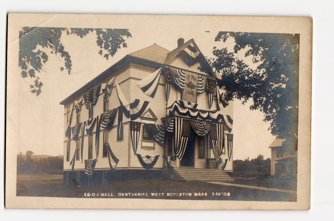 I.O.O.F. Hall Decorated for Centennial, West Boylston, Massachusetts, July 18, 1908 RPPC: The front of the postcard features a sepia-toned photograph of the I.O.O.F. Hall in West Boylston, Massachusetts, decorated for a centennial event on July 18, 1908. The two-story wooden building, with