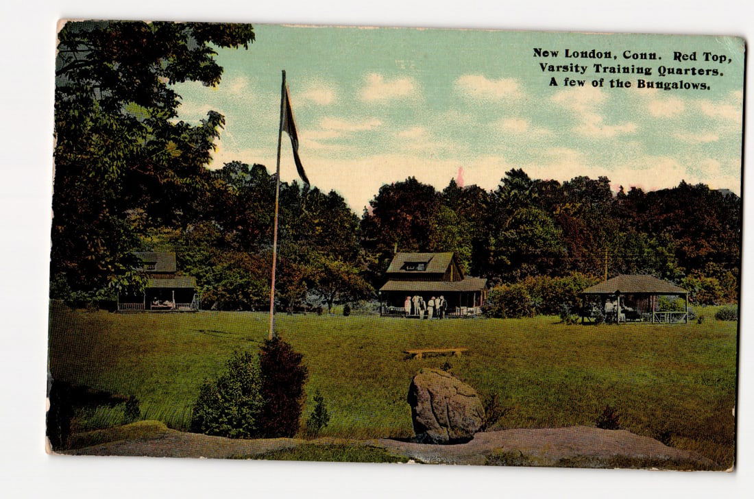 New London, Conn. Red Top, Varsity Training Quarters, A few of the Bungalows. Colorized View.: A colorized image depicts a landscape view of several wooden bungalows situated on a grassy expanse, with a dense treeline in the background under a partly cloudy sky. A flagpole displaying a flag (da