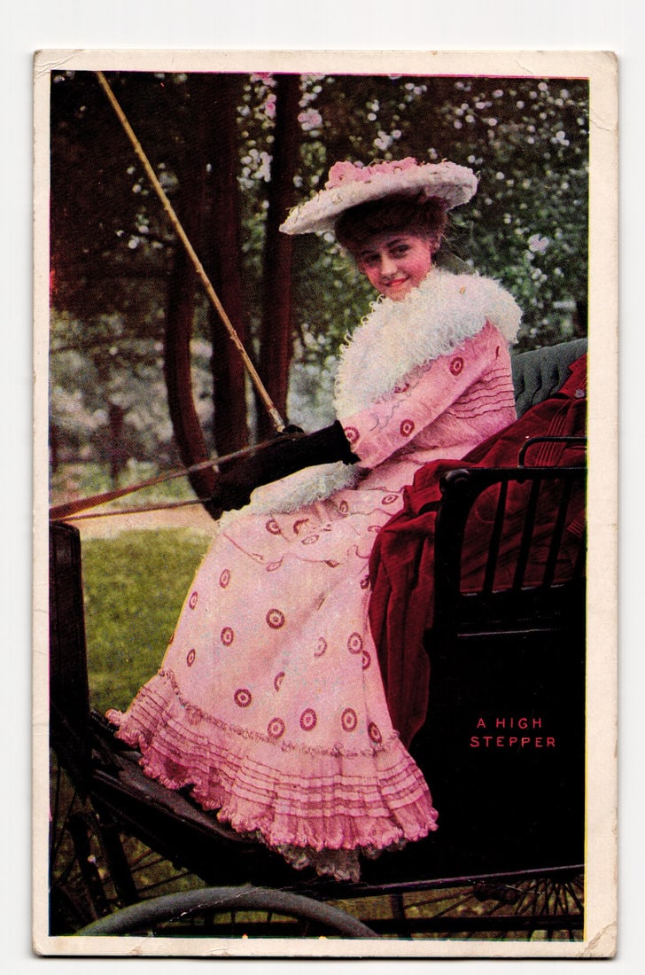 Colorized Postcard: Woman in Pink Dress & Hat in Carriage, "A High STEPPER", Postmarked 1907.: A colorized image shows a woman in a light pink, patterned dress with a white, fluffy collar, long black gloves, and a wide-brimmed, pink-adorned hat. She is seated in a dark carriage, looking at the