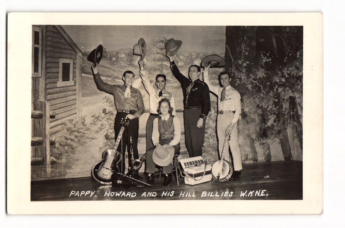 RPPC Pappy Howard and His Hill Billies W.M.N.E. Western Musical Group Portrait Postcard USA: This Real Photo Postcard (RPPC) displays a black and white photograph of the musical group "Pappy Howard and His Hill Billies". The ensemble, comprising five men and one woman, is posed on a stage in 