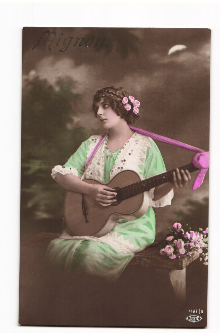 Postcard: "Mignon," Woman Playing Guitar, Hand-Tinted, K.u.K. Feldpost Censor Stamp, 1917: A hand-tinted photographic postcard. The front depicts a woman seated, turned slightly to her right, playing an acoustic guitar. She has dark, styled hair adorned with pink flowers and a dark circlet.