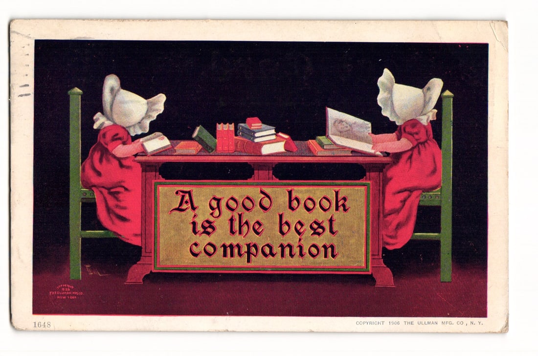 1906 Ullman Mfg. Co. Postcard: 'A good book is the best companion', Two Bonneted Figures Reading: A color illustration depicts two identical figures in profile, wearing white bonnets and red dresses, seated on green chairs at opposite ends of a long wooden table. Each figure is engrossed in readin