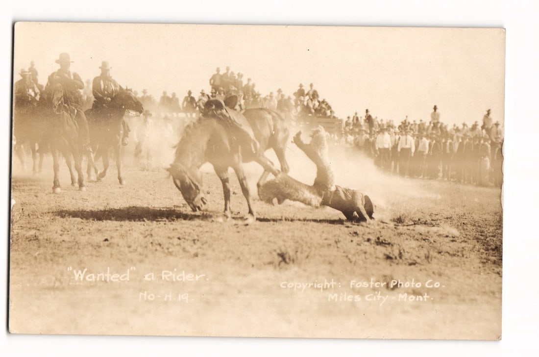 Rodeo Scene Postcard: "Wanted" a Rider, Bucking Bronco, Miles City, Montana, Foster Photo Co.: A sepia-toned photograph captures a dynamic rodeo scene. In the central foreground, a bucking bronco is captured mid-action, its rider in the process of being thrown and falling towards the dusty aren