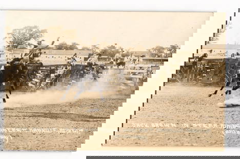 Postcard: Jack Brown, Steer Riding Contest, Arnville Round-Up (Hollenberg), Rodeo Action RPPC: A sepia-toned photograph captures an action scene from a steer riding contest. The central figure, a man, is depicted mid-ride on a bucking dark-colored steer within a dirt arena, with dust clouds kic
