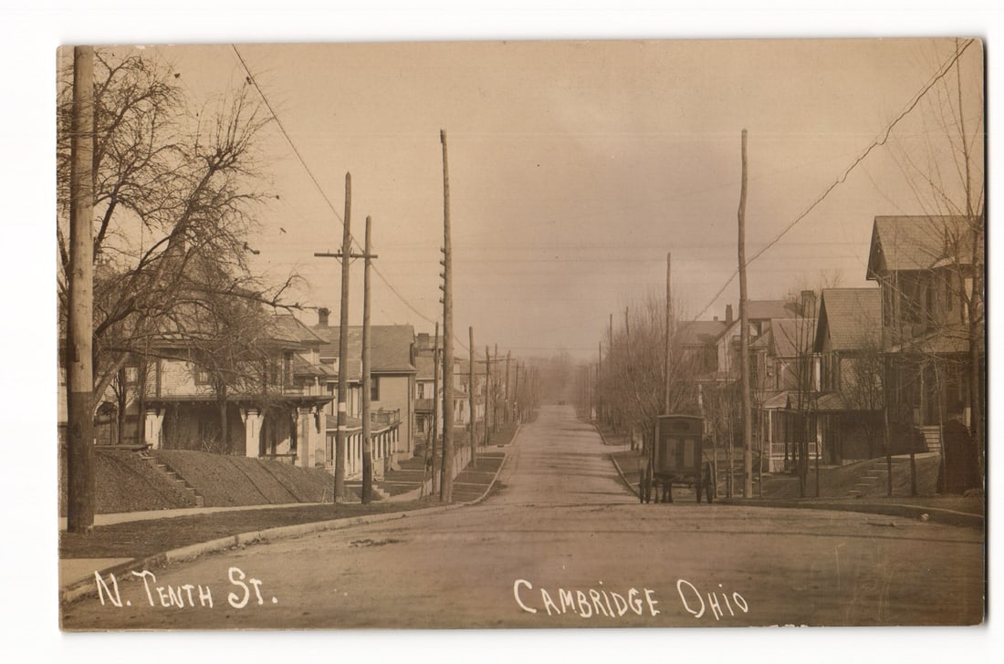 N. Tenth St., Cambridge Ohio, Residential Street View with Horse-Drawn Cart, Real Photo Postcard: A sepia-toned photographic image shows a view looking down N. Tenth St. in Cambridge, Ohio. The unpaved street recedes into the distance, flanked by two-story wooden houses with varied architectural s