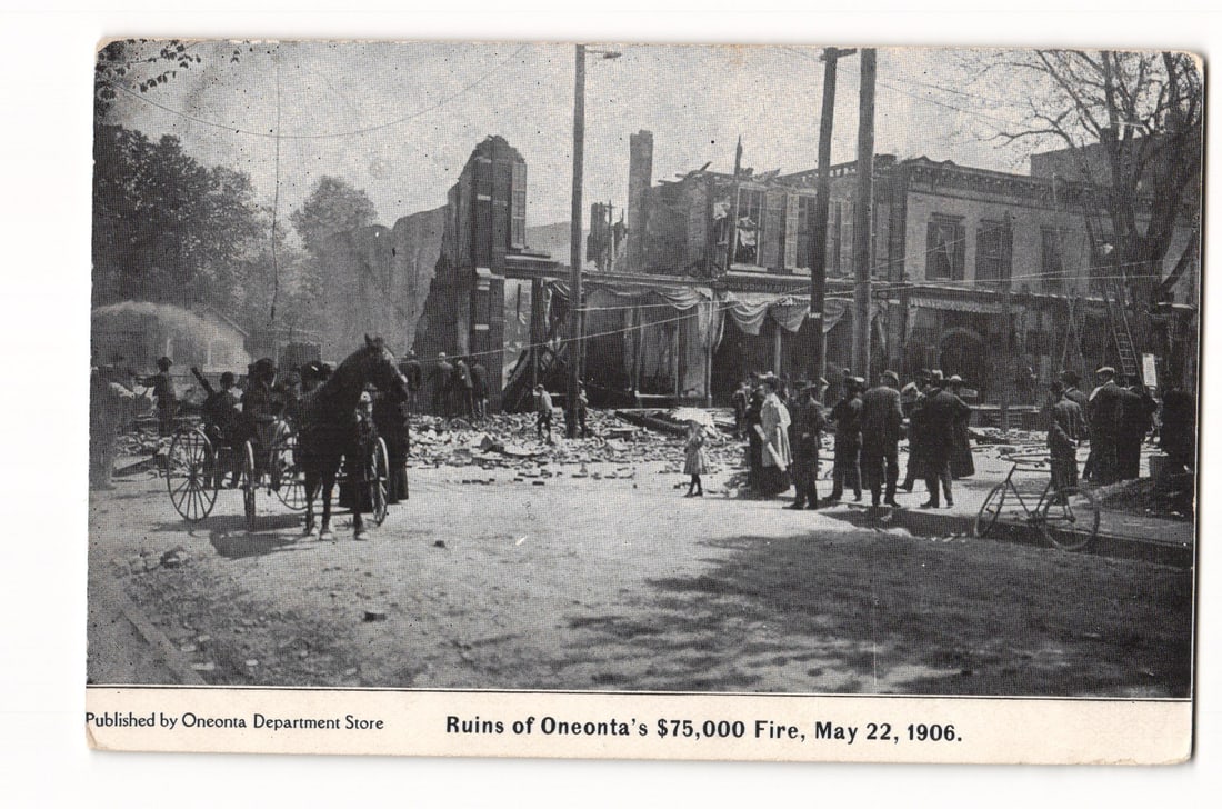 Ruins of Oneonta's $75,000 Fire, May 22, 1906, Crowd Viewing Aftermath, Halftone Postcard: A black and white halftone photographic print shows the aftermath of a fire. The image centers on the ruined structures of multi-story buildings, with some walls standing amidst widespread debris. A c