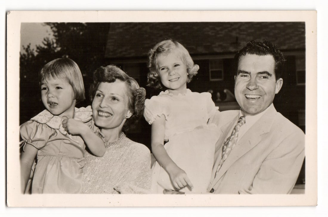Vintage Postcard: Richard Nixon, Pat Nixon & Daughters Family Portrait, Sent Sept. 29, 1952: A black and white photograph features a family group of four individuals. From left, a young girl with short, light-colored hair, wearing a patterned dress with a wide collar, is held by a smiling wom