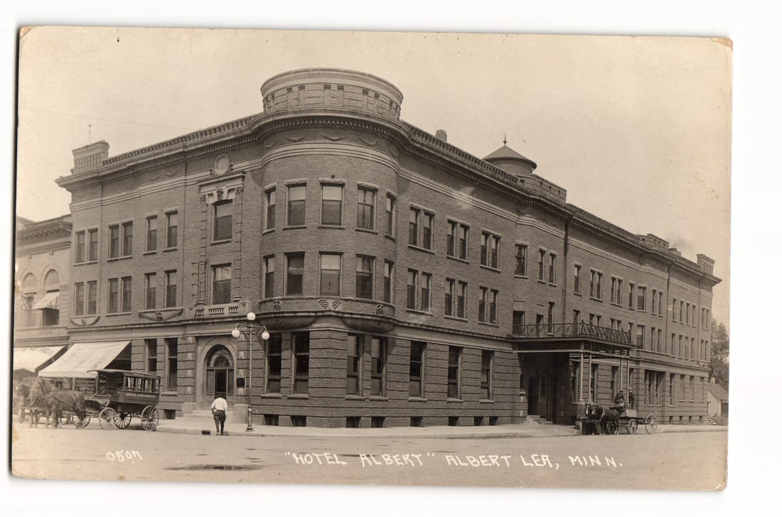 Hotel Albert, Albert Lea, Minnesota; Early 20th Century Sepia Photograph Postcard: A sepia-toned photographic postcard depicting the "Hotel Albert" in Albert Lea, Minnesota. The image shows a large, multi-story brick building with a prominent rounded corner featuring a turret-like s