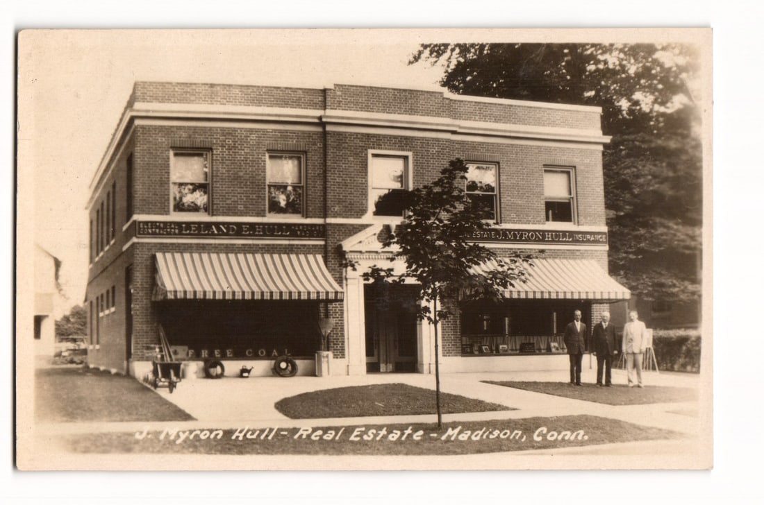 RPPC Postcard: J. Myron Hull Real Estate & Leland E. Hull Building, Madison, Conn. Advertising: A sepia-toned real photo postcard depicting a two-story brick commercial building, viewed from a slight angle to show the front and left side. The building features multiple rectangular windows on bot
