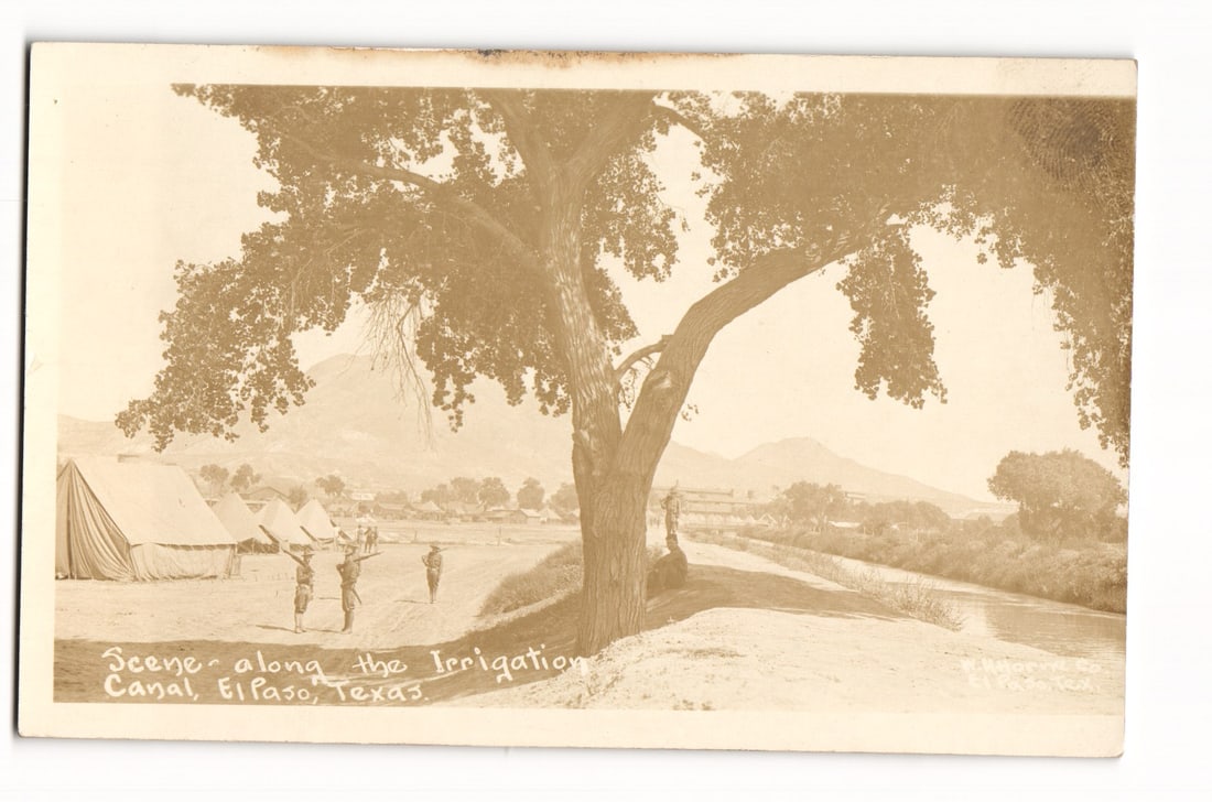 El Paso, Texas: Scene along Irrigation Canal, Soldiers, Military Encampment, RPPC postcard: A sepia-toned photograph depicts a scene dominated by a large, leafy tree in the center foreground. To the left of and slightly behind the tree, several figures, appearing to be soldiers carrying rifl