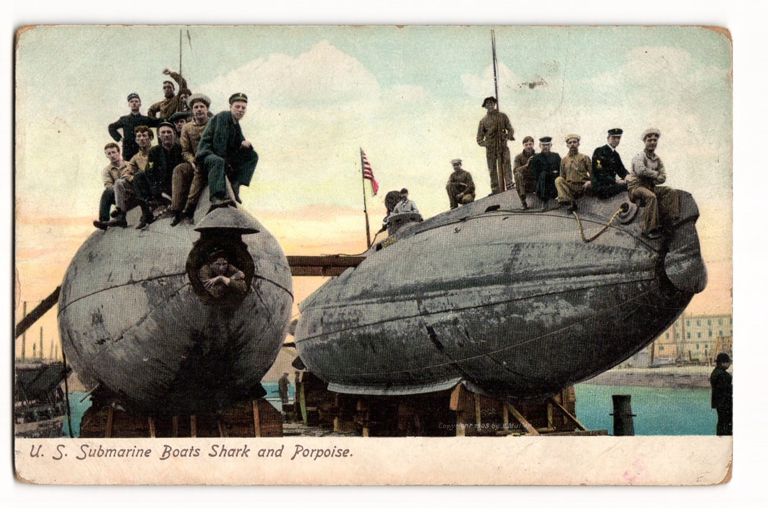 U.S. Submarine Boats Shark and Porpoise with Sailors, c.1905 Colorized Military Postcard: A colorized print, likely from a photograph, shows two U.S. submarines: "Shark" (left) and "Porpoise" (right), on wooden supports in a probable dry dock. Many sailors in early 20th-century uniforms ar