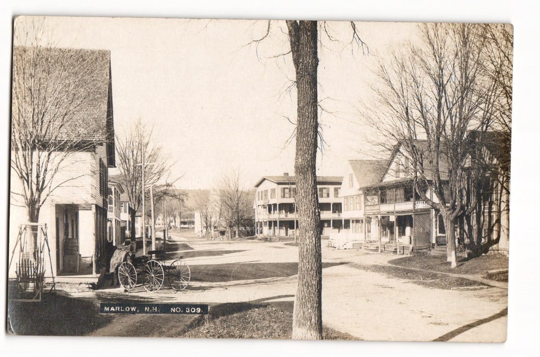 Marlow, New Hampshire Street Scene with Carriage, RPPC No. 309, Early 20th Century Postcard: A sepia-toned photographic image captures a wide, unpaved street in Marlow, New Hampshire. The perspective is eye-level, looking down the street. On the left, a two-story wooden building with shingle