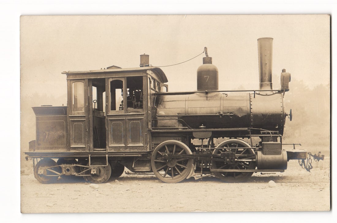 Real Photo Postcard Depicting Steam Locomotive No. 7 in Side Profile, Early 20th Century Style: A sepia-toned photograph depicts a steam locomotive, identified by the number "7" painted in a light color on its steam dome. The locomotive is shown in a right-facing profile, displaying its left sid