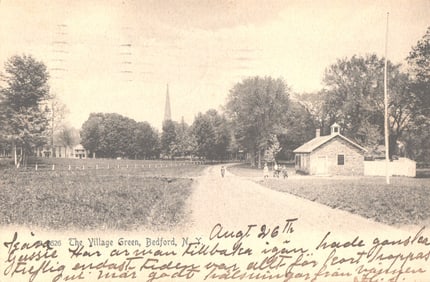Postcard view of The Village Green in Bedford, New York with dirt road and stone building. Posted