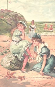 Embossed postcard of young women in Edwardian dresses on a seaside beach, one helping with a shoe.