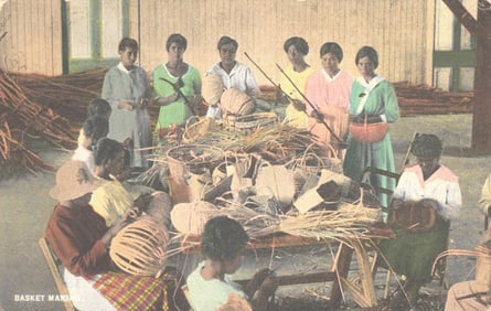 Postcard view of Jamaican women and children making woven baskets in Kingston, Jamaica, circa 1920s.