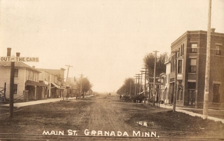 RPPC Main Street view in Granada, Minnesota showing muddy roads and early automobiles sign c. 1909.