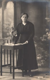 RPPC Real Photo Postcard studio portrait of a woman in dark Edwardian dress beside a table with