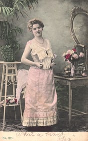Postcard of an Edwardian era woman getting dressed, lacing up her corset in a studio setting. c.1906