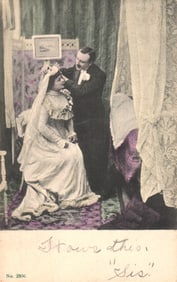 Edwardian era postcard of a groom adjusting the veil on his seated bride in a studio setting c.
