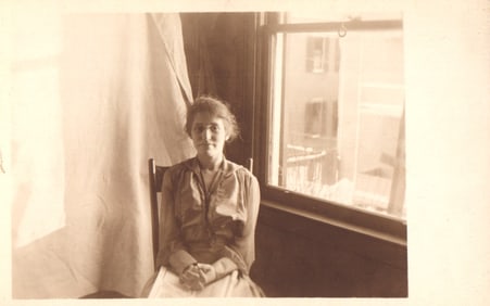 RPPC Real Photo Postcard of a young woman with glasses seated by a window, indoor portrait c. 1910s