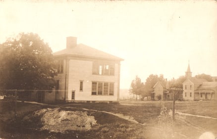 RPPC Real Photo Postcard view of a large two-story schoolhouse in a rural American town setting.