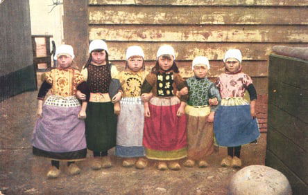 Early 1900s postcard showing a group of six young girls in traditional Dutch folk costumes & clogs.