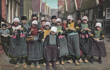 Color postcard of Dutch children in traditional costumes & clogs knitting on a street in Marken,