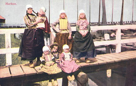 Postcard view of women and children in traditional folk dress of Marken, Holland, posing on a wooden