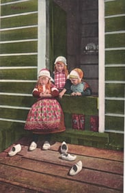 Postcard of three children in traditional Dutch costumes and clogs sitting on a stoop in Marken,