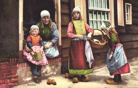 Photochrom postcard of a woman and three girls in traditional Dutch folk costumes and clogs in
