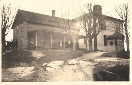 RPPC Real Photo Postcard showing a large two-part wood frame house with men on the porch, c. 1910s.