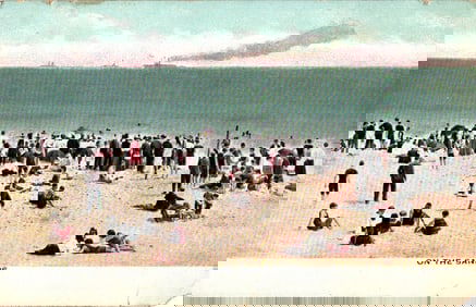 Postcard showing a busy beach scene 'On The Sands' with crowds of people in Edwardian attire, 1909