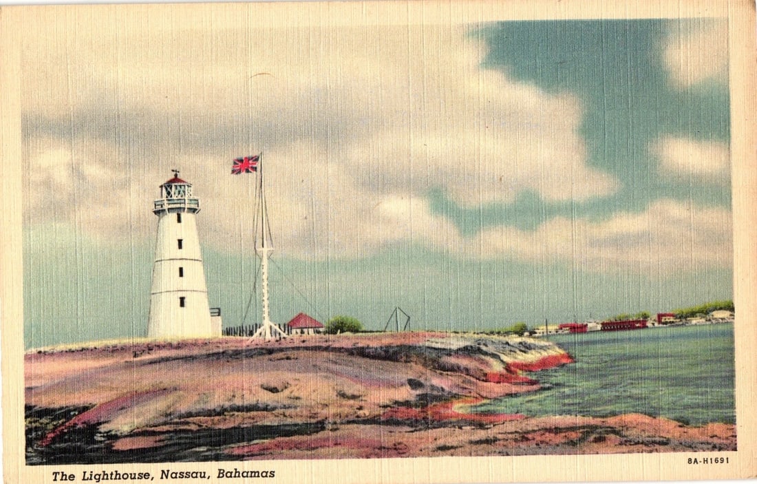 Early-Mid 20th Century Postcard: The Lighthouse, Nassau, Bahamas, with British Flag: A vibrant colorized photochrome postcard depicting The Lighthouse in Nassau, Bahamas. The white lighthouse, topped with a red element, stands on a rocky, reddish-brown promontory at the left. Adjacent