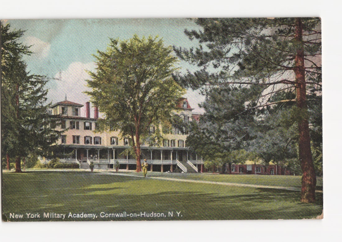 Early 20th Century View of New York Military Academy in Cornwall-on-Hudson Postcard: A multi-story institutional building, likely a dormitory or main hall, with a wide porch or balcony extending along its front facade, is centrally positioned to the left. The building features numerou