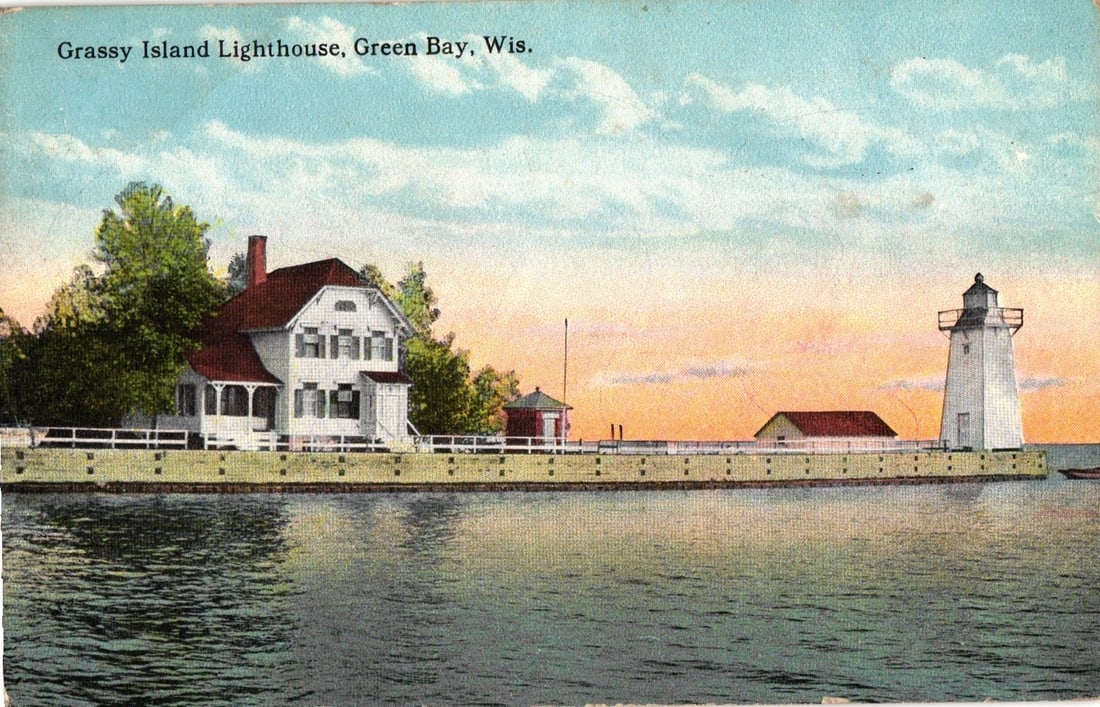 Grassy Island Lighthouse, Green Bay, Wisconsin, circa 1923 color lithograph view postcard.: The Grassy Island Lighthouse complex is depicted, featuring a multi-story white building with a red roof and porch, an adjacent small red-roofed structure, and a cylindrical white lighthouse tower wit