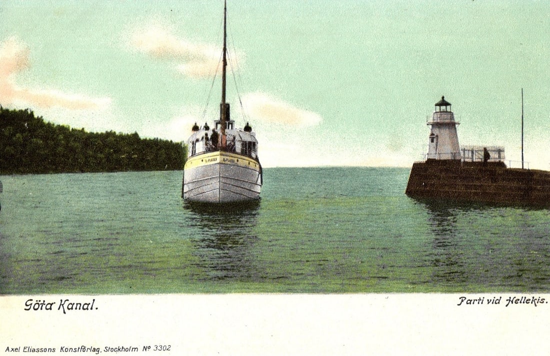 Passenger Steamboat and Lighthouse on Gota Canal at Hellekis, Sweden early 20th century postcard: A passenger steamboat, identified as 'GOTA' on its side, navigates a waterway. The white-hulled vessel, positioned centrally, has a prominent mast and several individuals visible on its upper deck. To