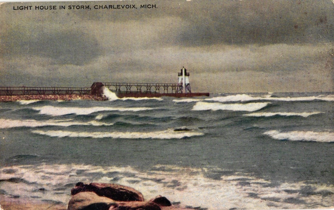 Stormy Weather Lighthouse on Pier Postcard in Charlevoix, Michigan, Early 20th Century: A color lithograph postcard depicts a lighthouse standing on a pier or breakwater amidst a storm. Rough waves with whitecaps crash in the foreground and midground, with dark, heavy clouds filling the 