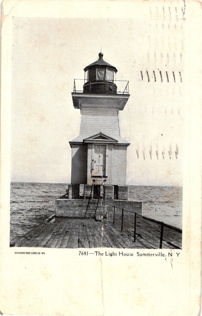 Early 20th Century Lighthouse, Summerville, New York, 1906 Postcard with Waterfront View: A photographic postcard depicts a lighthouse centered in the frame, viewed from a slightly low perspective. A wooden pier or walkway extends from the foreground directly towards the lighthouse, which 