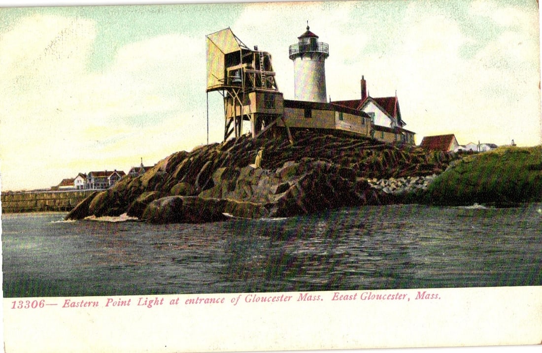 Eastern Point Light Lighthouse at Entrance of Gloucester, Massachusetts Lithograph Postcard: Eastern Point Light, situated on a rocky promontory at the entrance of Gloucester, Massachusetts, is the primary subject. The image depicts a cylindrical lighthouse tower with a lantern room, connecte
