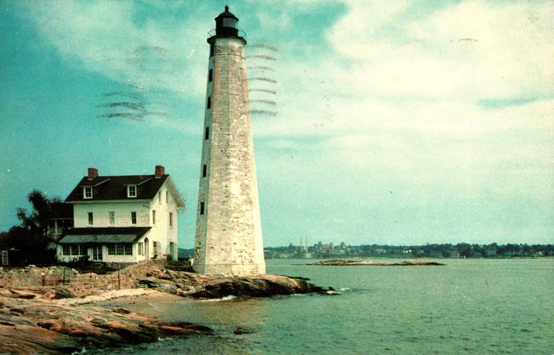 Historic New London, Connecticut Lighthouse and House on Rocky Shore Vintage Postcard: A tall white lighthouse with a black top stands on a rocky shore beside a large white house with dark roofs and chimneys. The structures are positioned near a body of water, with faint land visible on