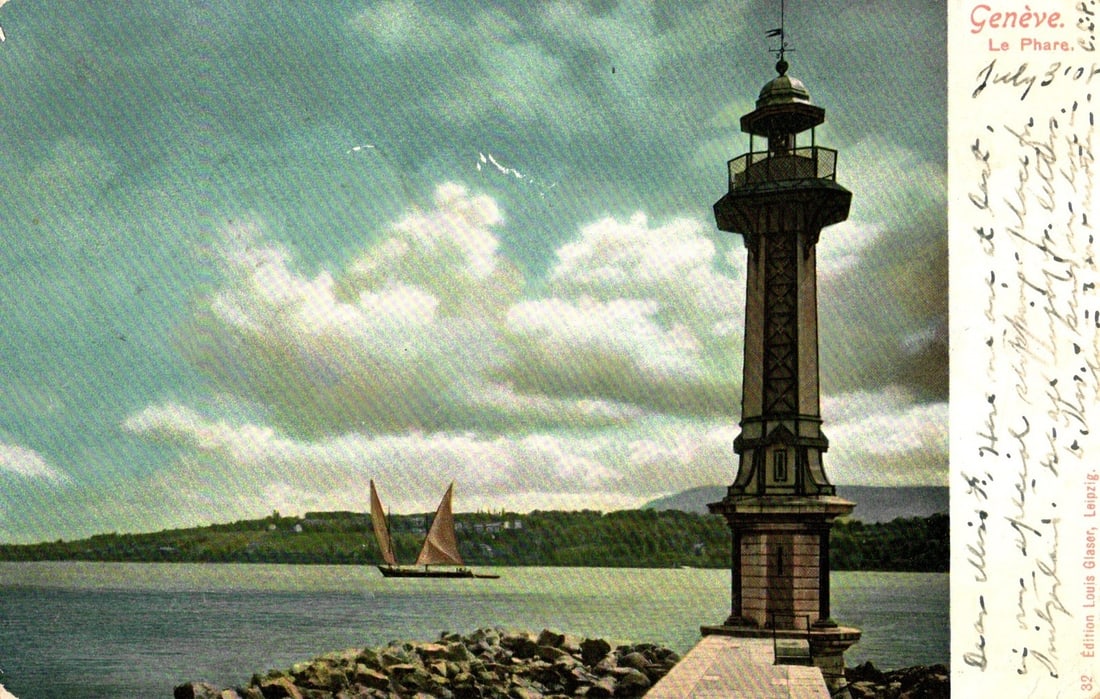 Early 20th Century Postcard of Le Phare Lighthouse and Sailboat, Lake Geneva, Switzerland: A scenic chromolithograph postcard depicts Le Phare lighthouse on the right, rising from a rocky shore into a partly cloudy sky. The lighthouse features a stone base and an ornate dark latticework tow